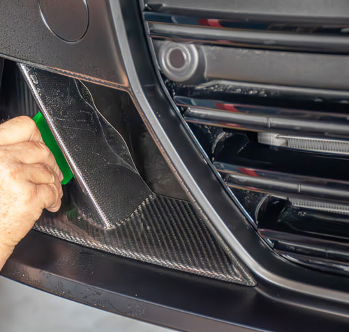 Technician applying XPEL Stealth Paint Protection Film to a matte graphite car bumper