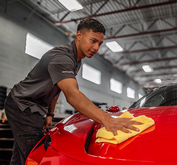 Technician applying Paint Protection Film (PPF) to a red sports car at The Specialists in Tucson